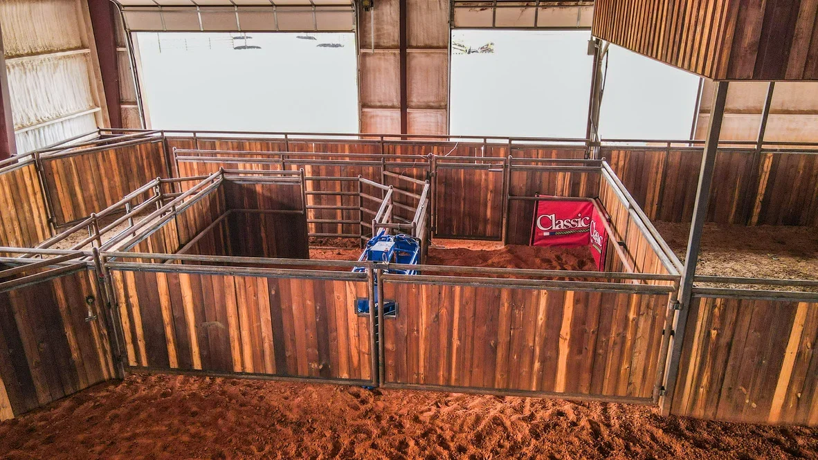 Wooden horse stalls with metal framing, vertical wood siding, and sand footing in covered facility
