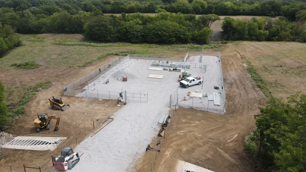 Aerial view of concrete foundation pad with gravel road, fencing, and excavation equipment on cleared site
