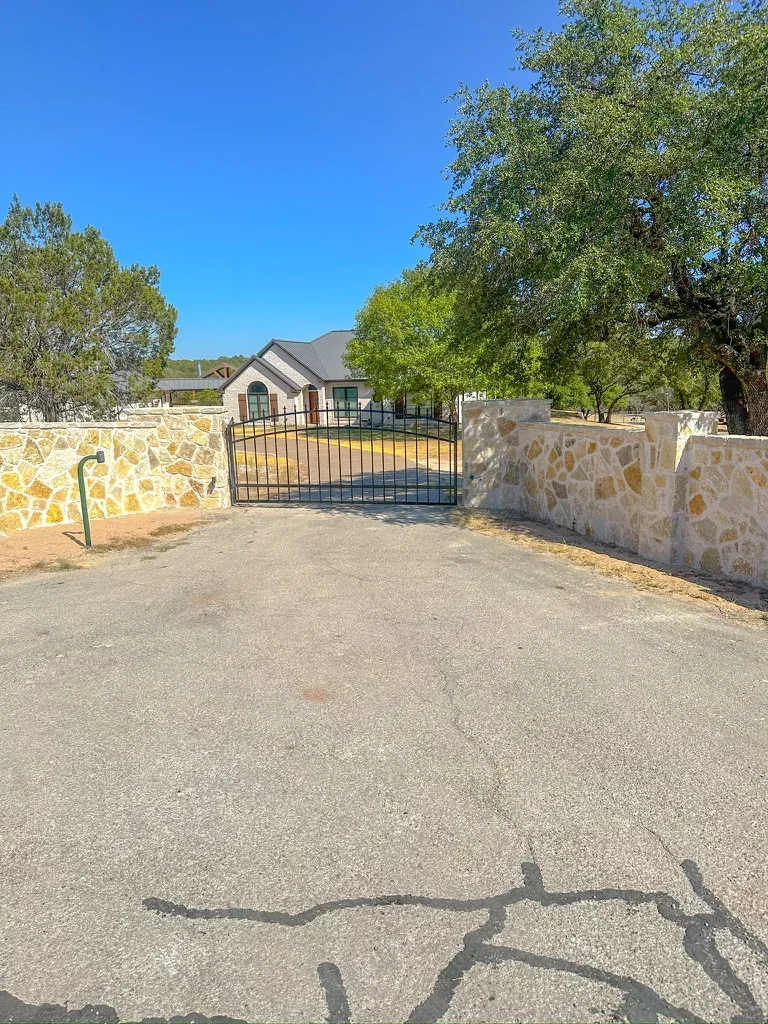 Stone pillar entry gate with black metal gate on gravel driveway, stacked stone construction