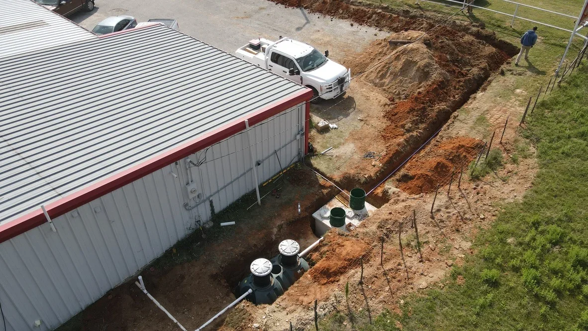 Septic tank installation with concrete chambers, excavated trench, and drainage piping near metal building