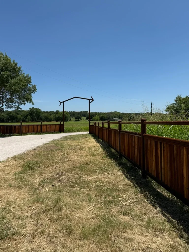 Stained wood fence with metal arbor gateway and gravel driveway on rural property