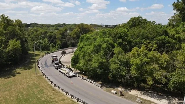 Curved asphalt highway with metal guardrails through wooded area, heavy equipment on road