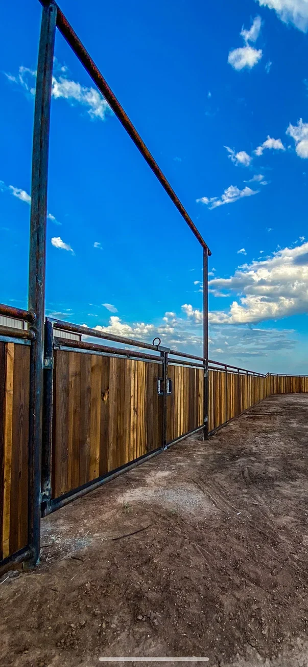 Steel frame corral fence with wooden panels and swing gate in dirt arena