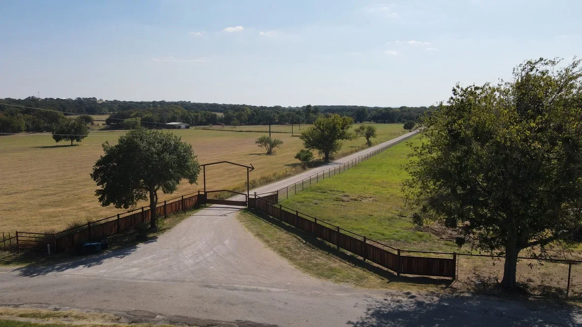 Graded driveway with metal entrance gate and wooden ranch fencing on rural property