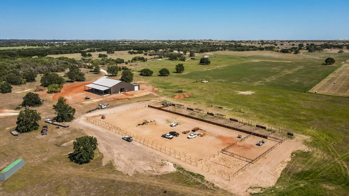 Aerial view of excavated agricultural site with metal barn, livestock pens, and graded dirt work