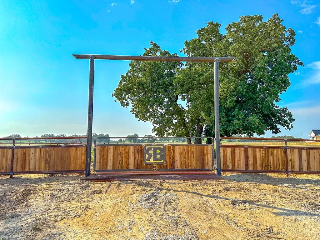 Steel frame ranch gate with wood panels and yellow emblem on rural property