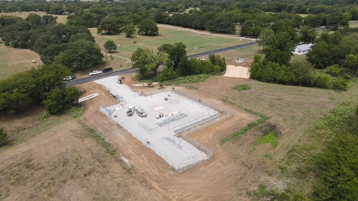 Aerial view of excavated commercial foundation pad with concrete base, rock perimeter, and cleared site access