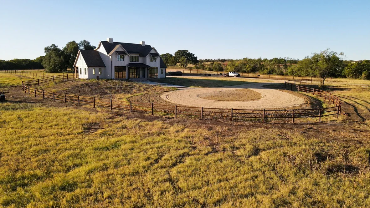 Circular equestrian arena with compacted footing, metal rail fencing, and graded earthwork on rural property