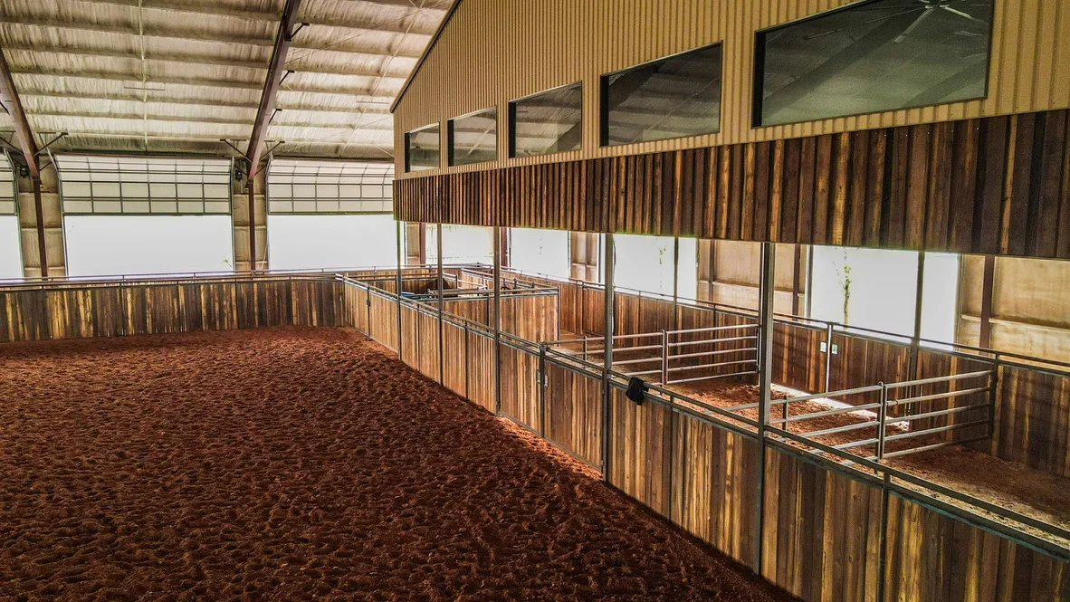 Indoor arena with metal frame, corrugated roof, wooden fencing, and compacted arena footing