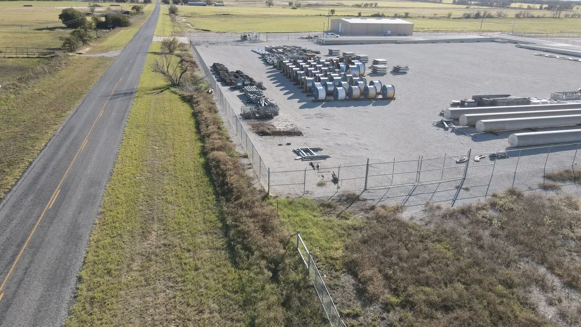 Aerial view of excavated industrial yard with concrete pad, material storage, and perimeter fencing