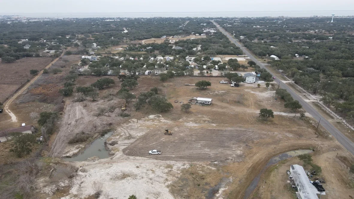 Aerial view of excavated land clearing with graded earth, retention pond, and heavy equipment on rural property