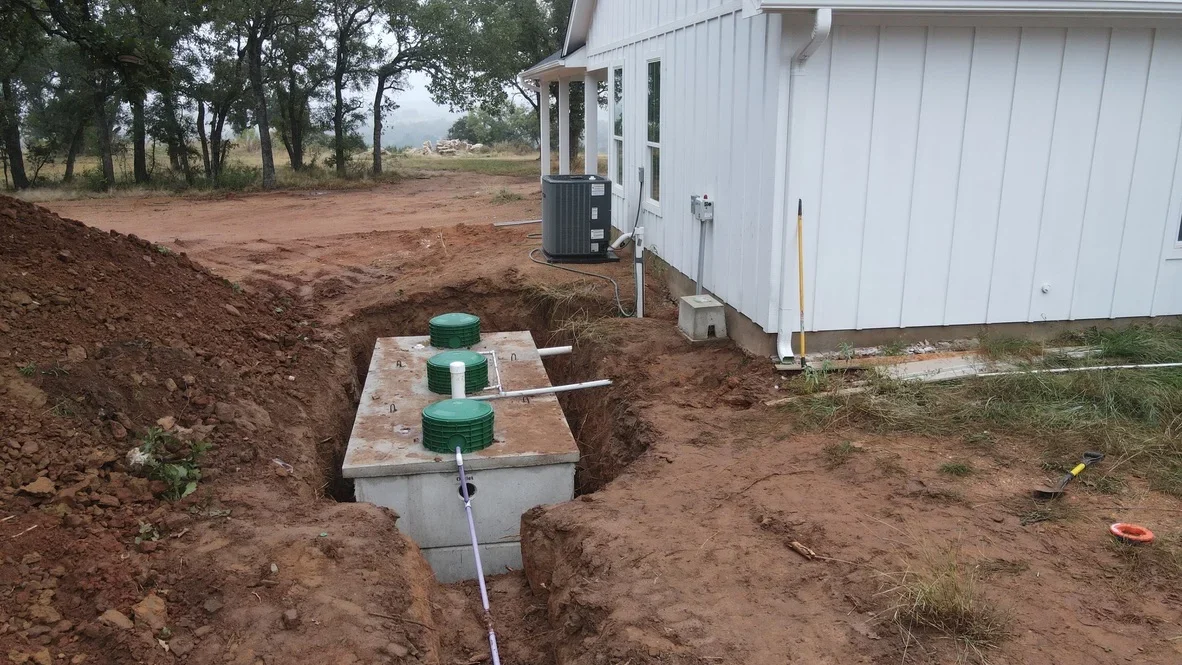 Concrete septic tank with green access covers installed in excavated trench with PVC piping connections