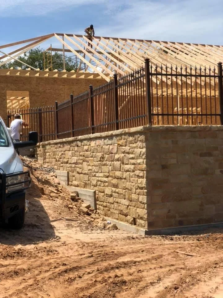 Stone retaining wall with metal fence and timber roof framing during residential excavation project