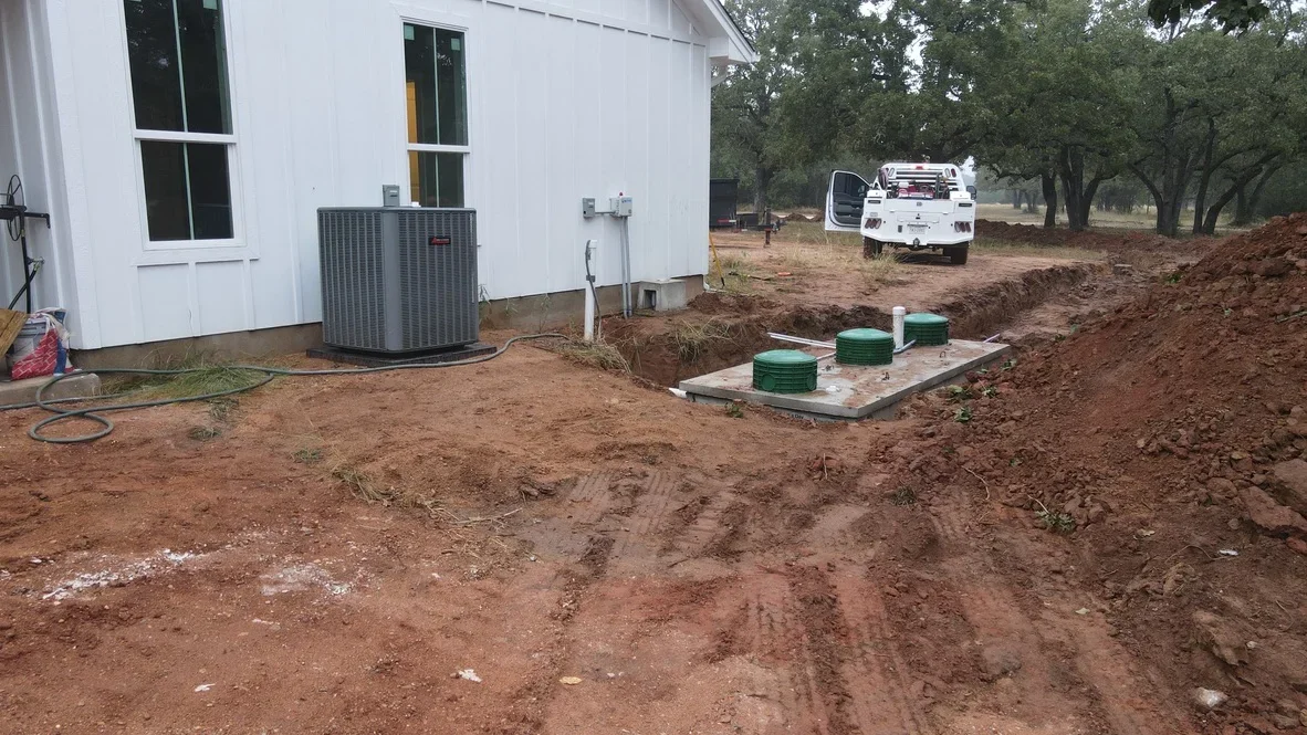 Septic tank installation on concrete pad with excavated site preparation and HVAC unit visible