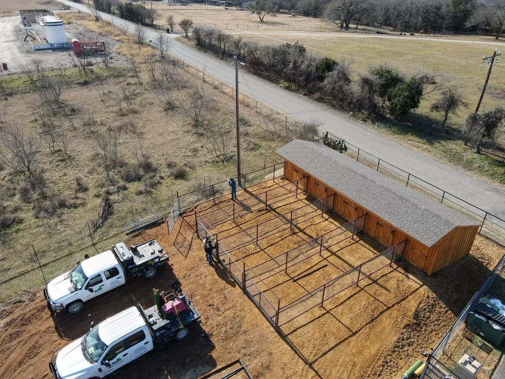 Metal corral with pipe fencing, wooden shelter with metal roof, and graded earthwork on rural property
