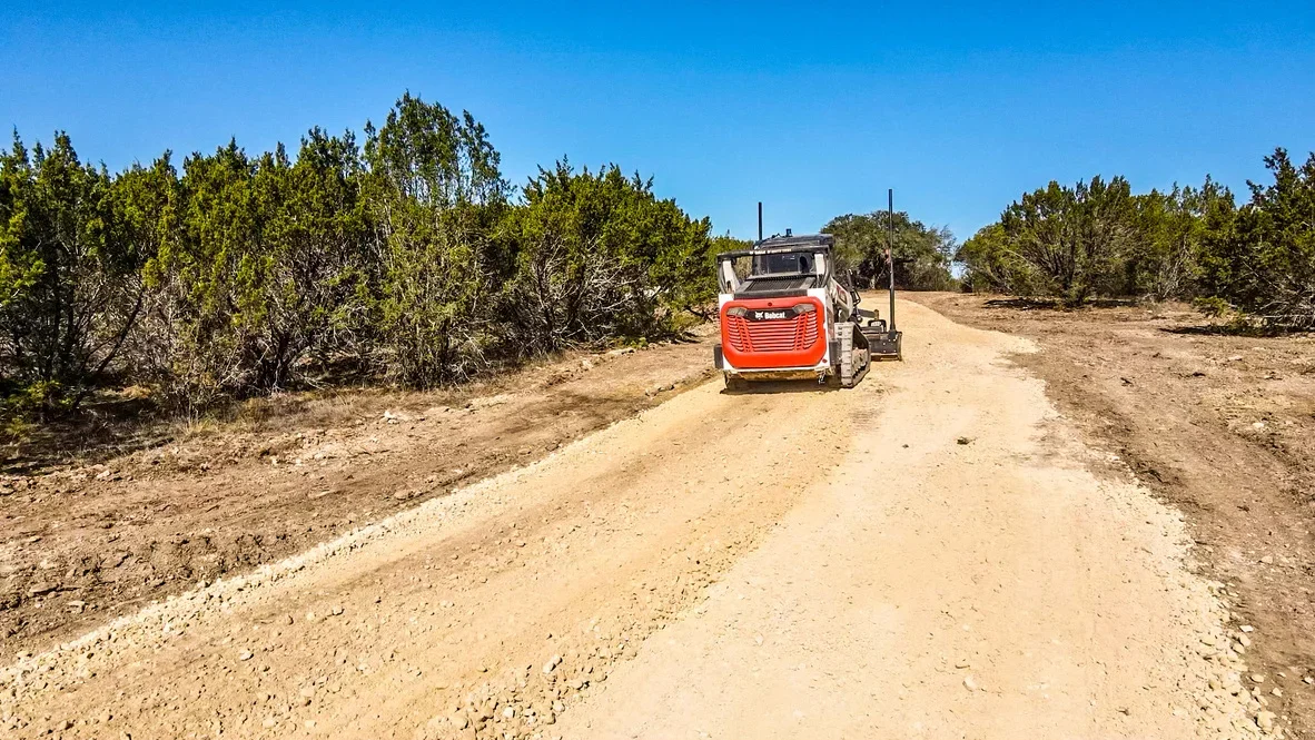 Red Bobcat truck on newly graded gravel driveway with cleared vegetation on both sides