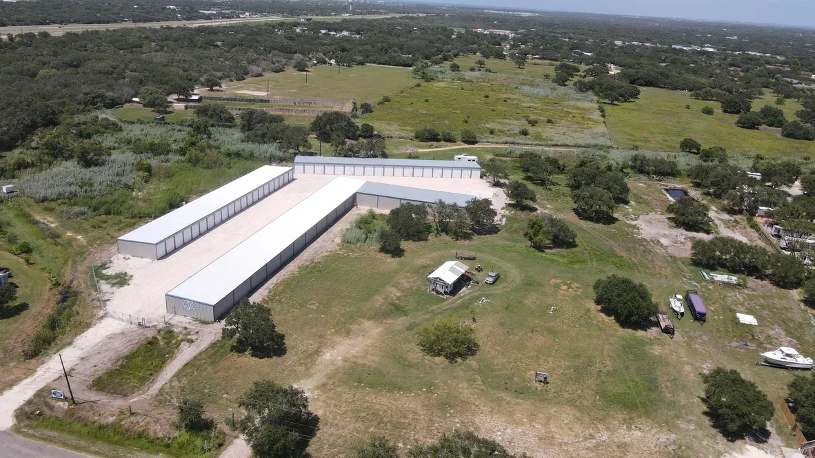 Two large metal storage buildings with white roofs on graded site with access roads and cleared grounds