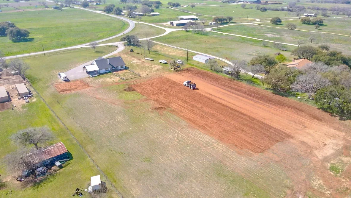 Aerial view of excavated residential lot with red clay soil, cleared land, and grading equipment on property