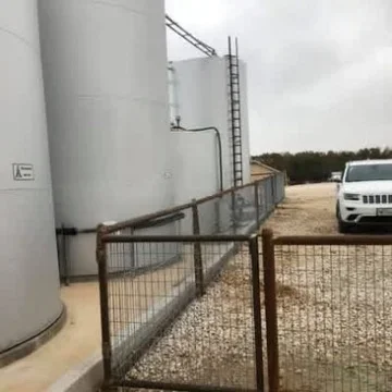 White cylindrical storage tank on gravel pad with metal ladder and safety fence installation