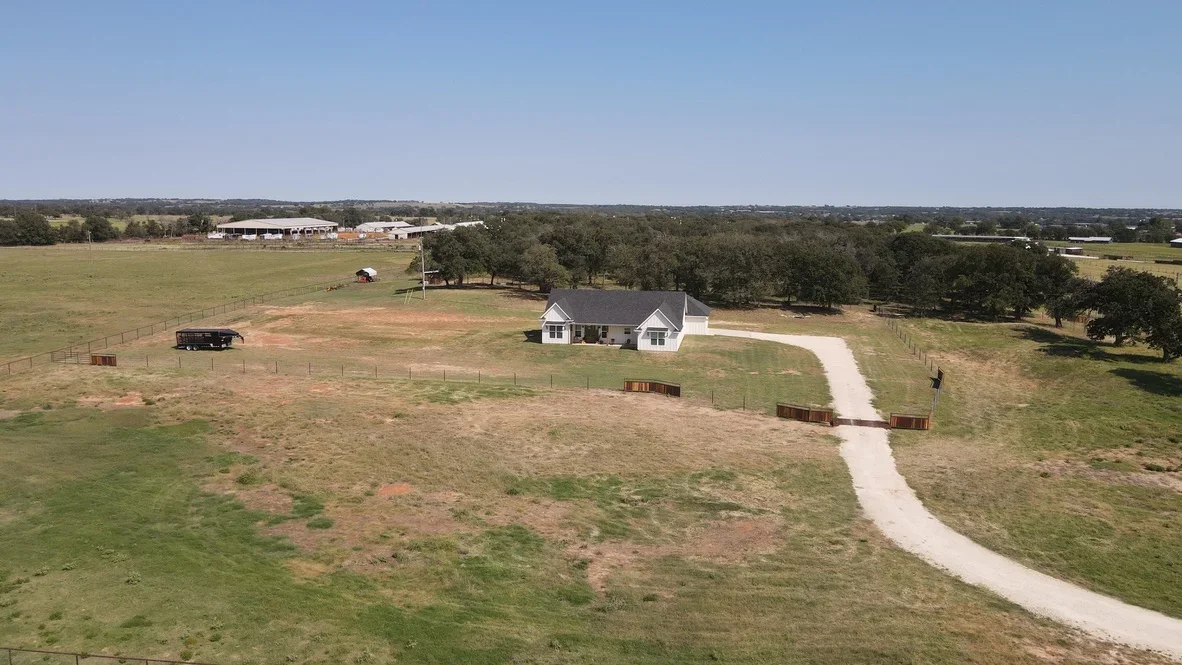 Gravel driveway with metal gates leading to white ranch house on rural property