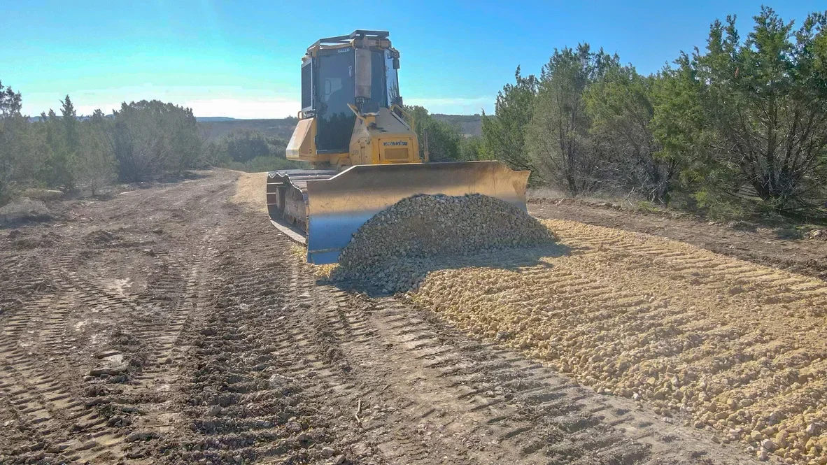 Compact track loader spreading crushed rock aggregate on graded driveway base