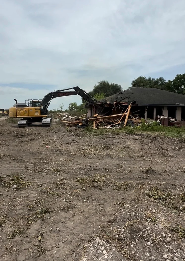 Excavator demolishing residential building frame with exposed wood structure and debris