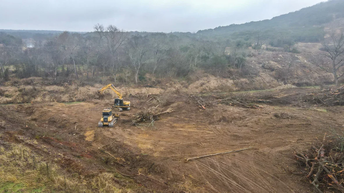 Excavators and dozers clearing trees and grading sloped terrain with removed timber and debris