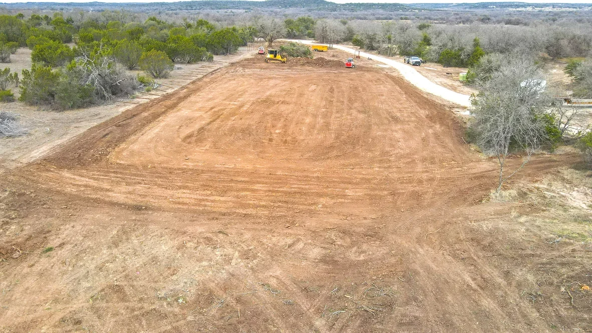 Aerial view of excavated site with large dirt mound, graded slopes, and heavy equipment during active earthwork operations