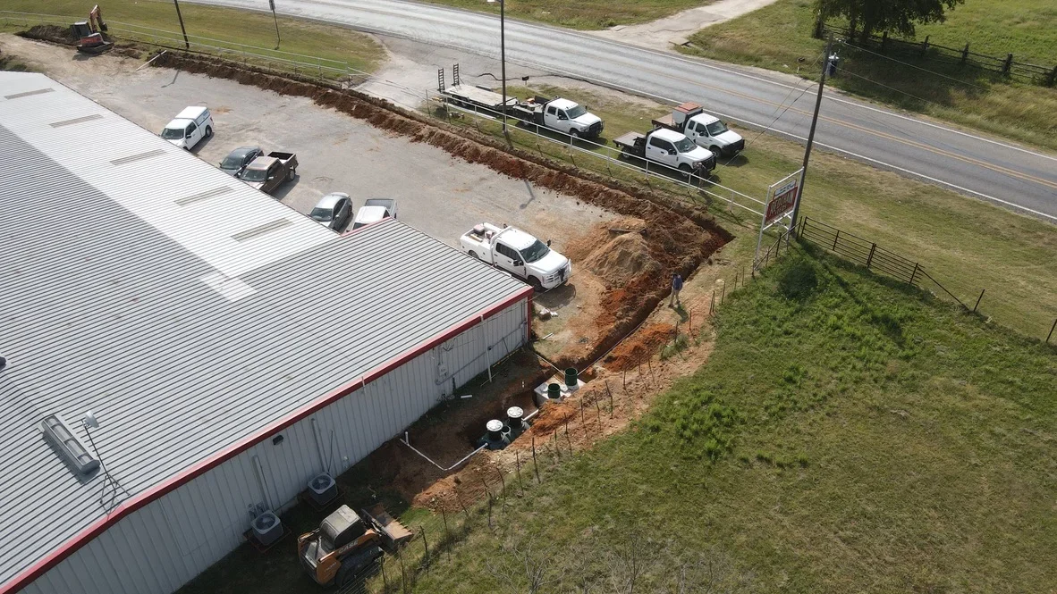 Aerial view of excavation work with heavy equipment, exposed soil, and graded earth at commercial site