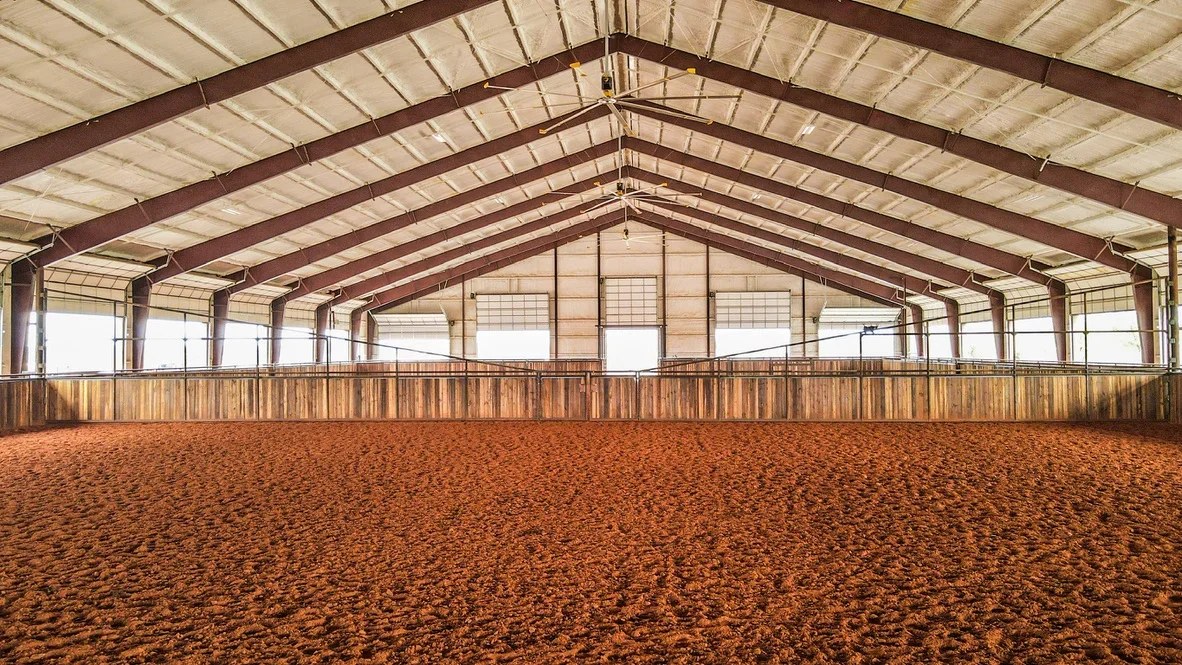 Indoor equestrian arena with compacted arena floor, steel frame, and wooden perimeter fencing