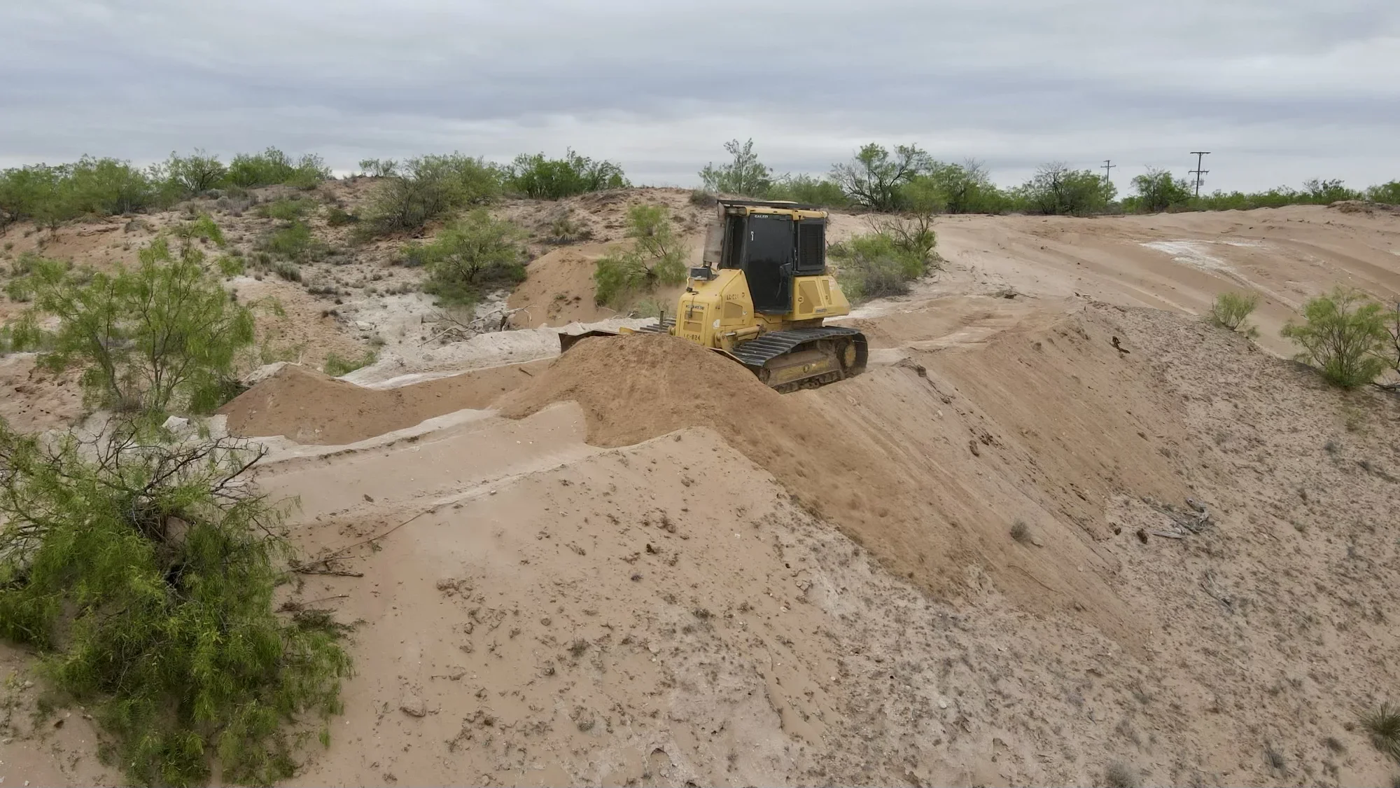 Yellow tracked dozer grading and moving earth on large undeveloped property with sparse vegetation