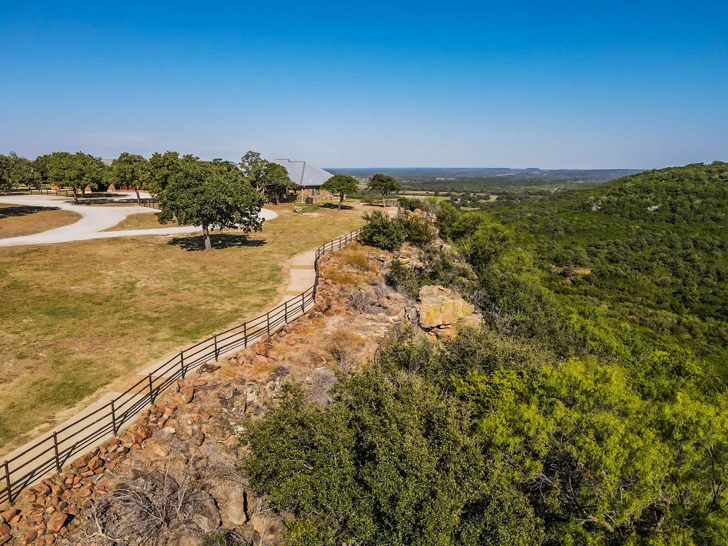 Metal ranch fencing along rocky hilltop with graded pathways and mature trees