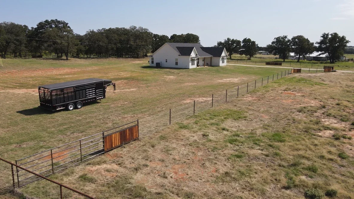 Steel pipe fencing and gates installed on rural ranch pasture with livestock trailer and house in background