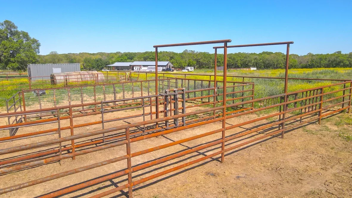 Steel pipe livestock corrals with working pens, loading chute, and compacted earth base on rural property