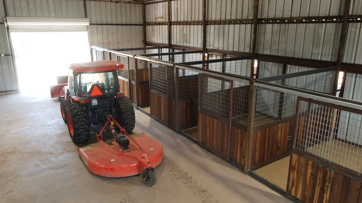 Steel-frame agricultural building with wire mesh stalls, wood panels, and concrete floor