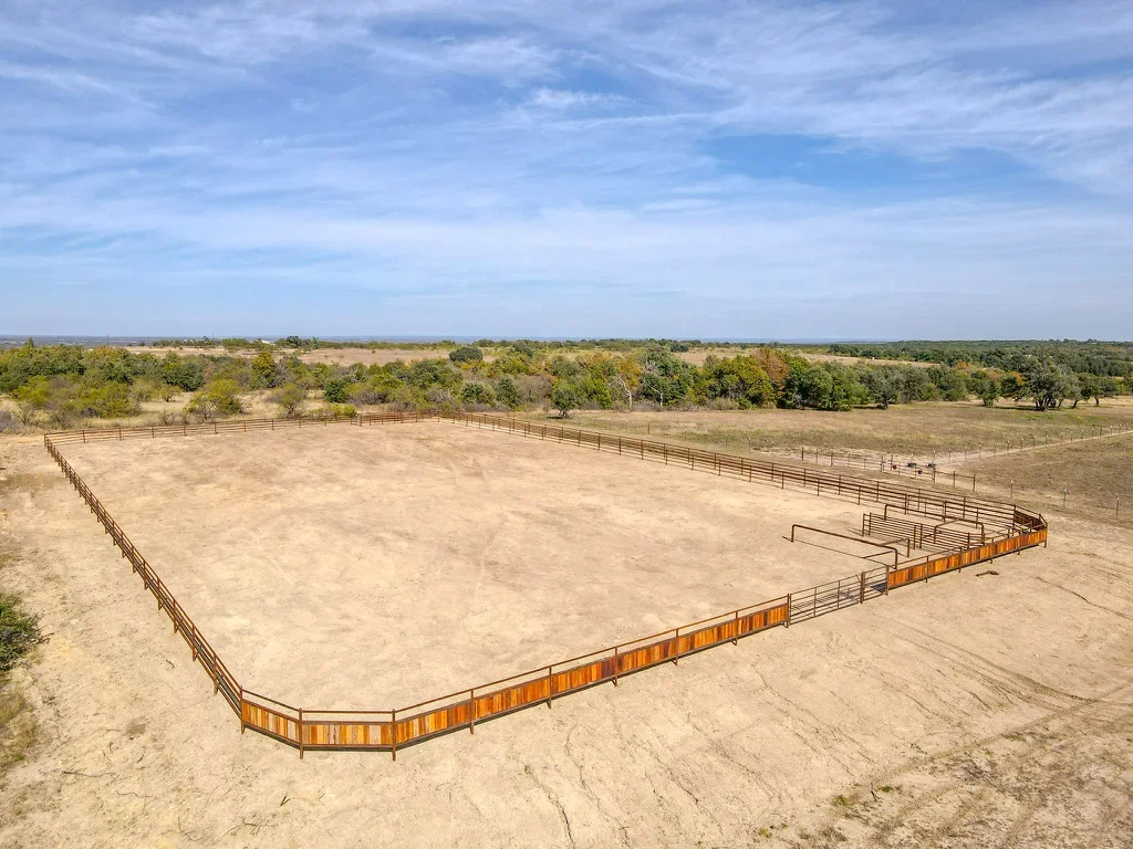Aerial view of excavated arena with metal pipe fencing and compacted dirt surface