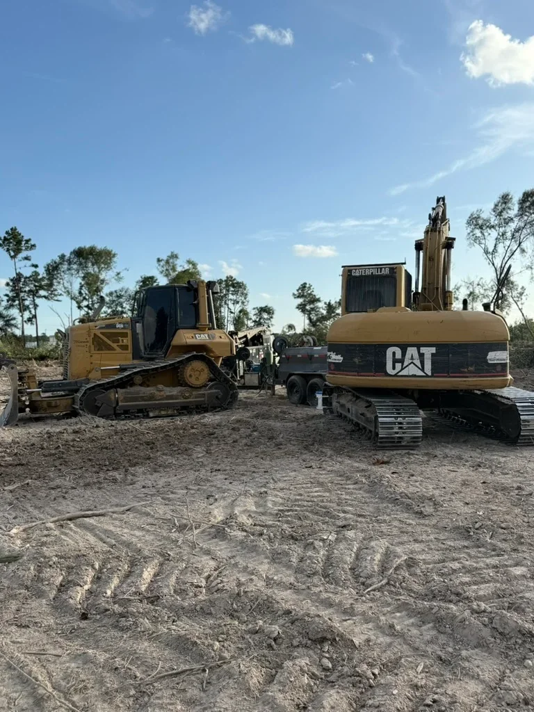 CAT dozer and excavator on cleared dirt site with equipment staging area