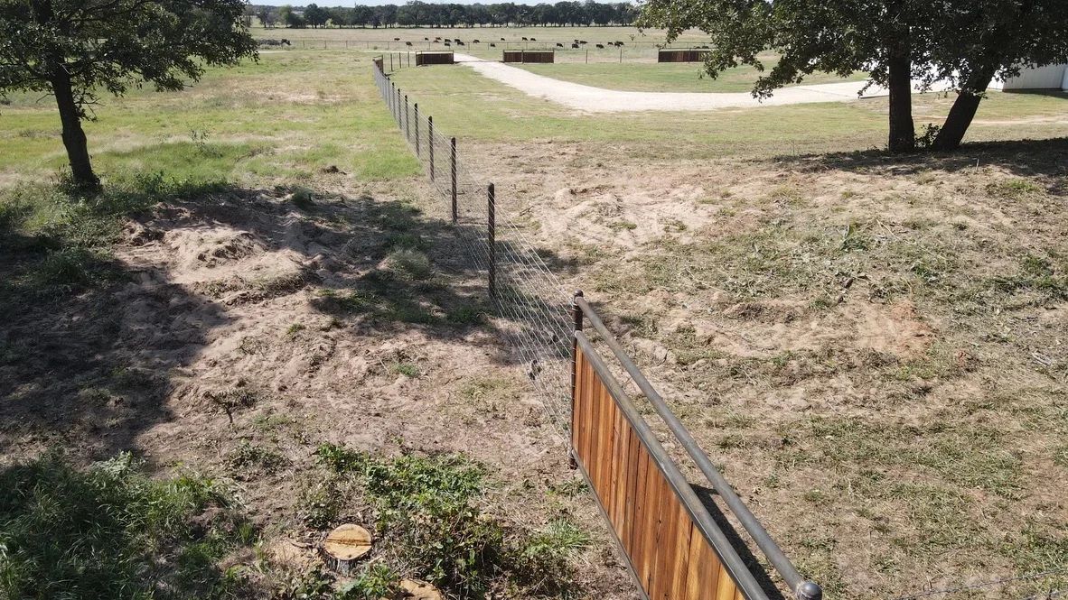 Wood and wire mesh ranch fencing with metal posts installed across pasture with mature oak trees
