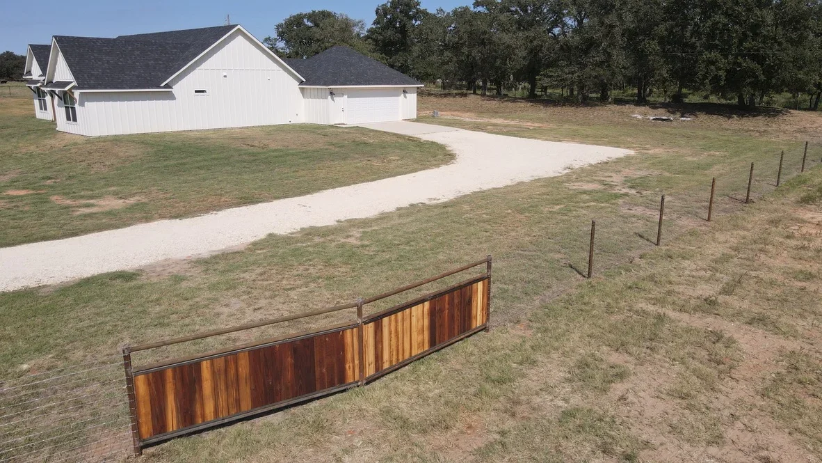 Curved concrete driveway with graded property, metal ranch fencing, and white residential home