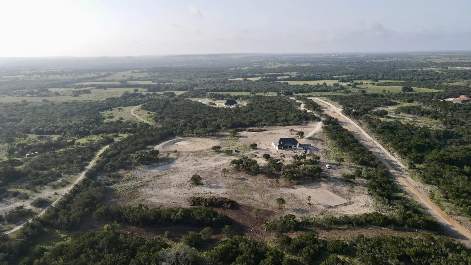 Aerial view of excavated residential site with graded earth, access road, and cleared building area surrounded by timber