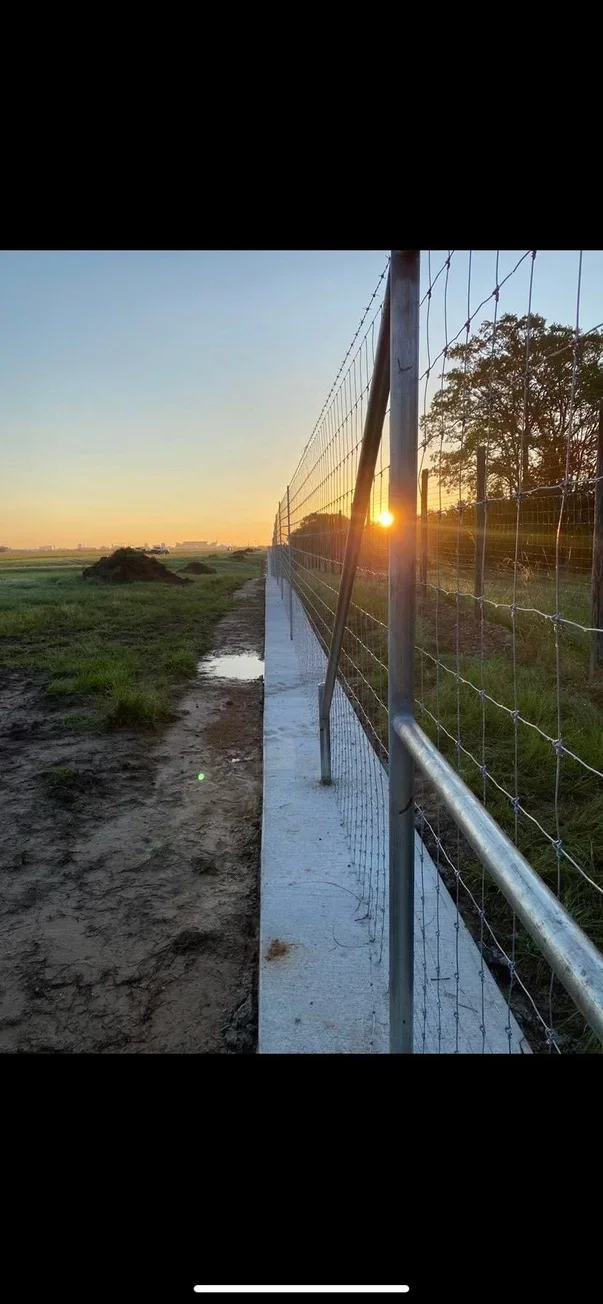 Metal post and wire fence with horizontal rails installed across pasture at sunset