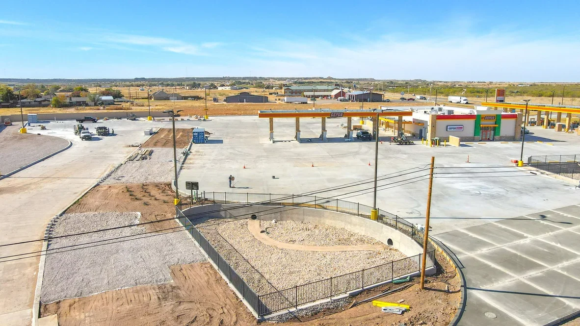 Aerial view of commercial excavation site with graded concrete pads, metal fencing, and heavy equipment