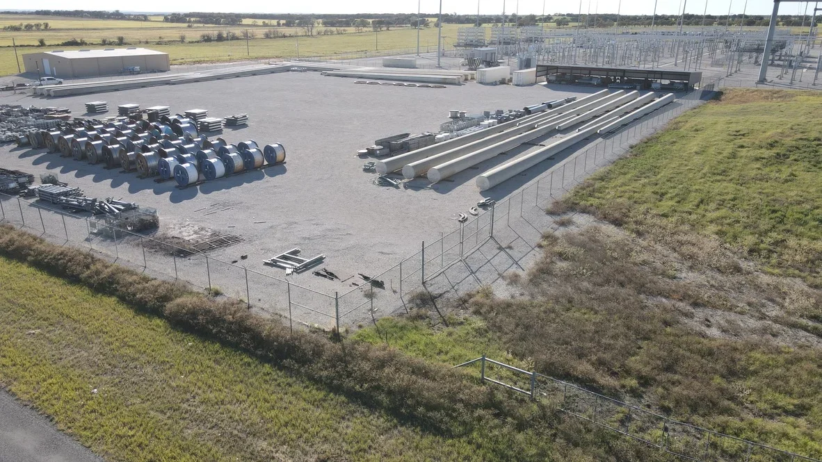 Excavated industrial yard with concrete pad, steel material storage, and perimeter fencing