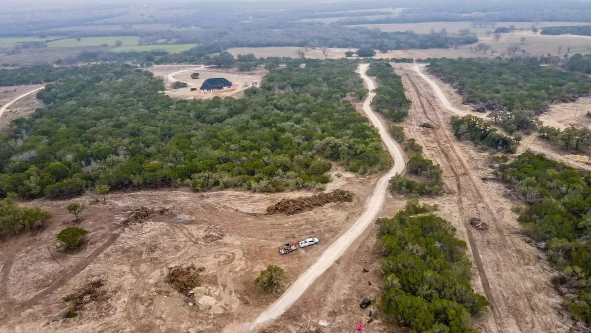 Aerial view of excavated rural property with graded roads, cleared building site, and preserved tree stands