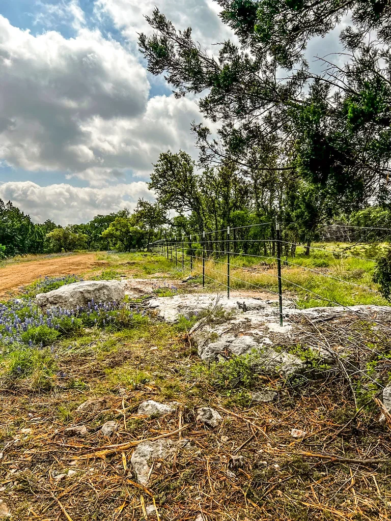 Metal pipe fence with wire fencing installed on rural property with limestone outcrops and native trees