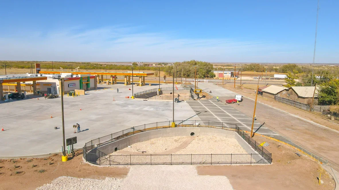 Aerial view of excavated basin with metal railings, concrete pad, and graded commercial site