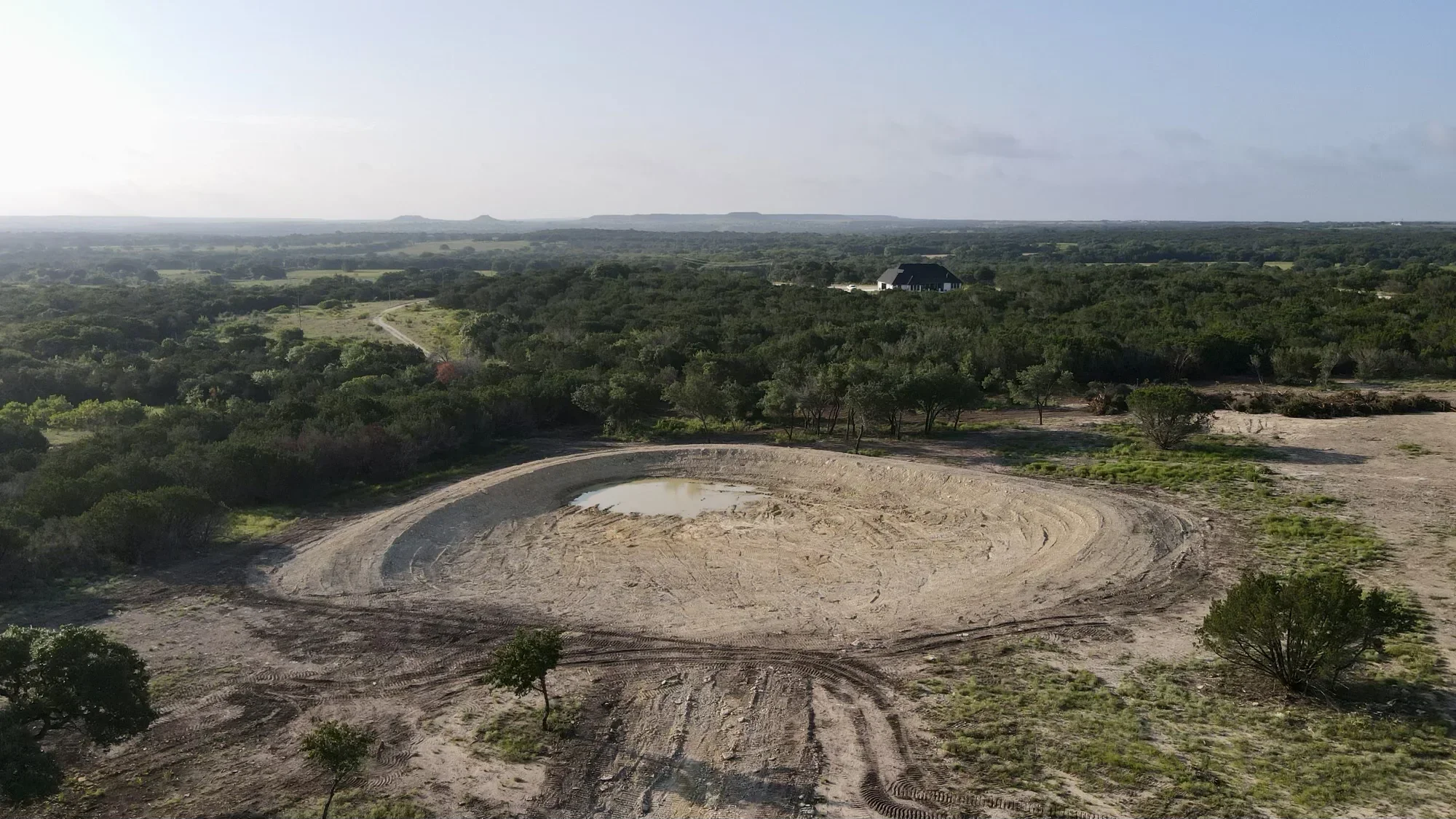 Aerial view of completed pond excavation with compacted earthen dam and cleared surrounding land