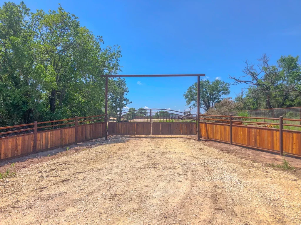 Wood post-and-rail corral fencing with metal gate frame and gravel arena floor