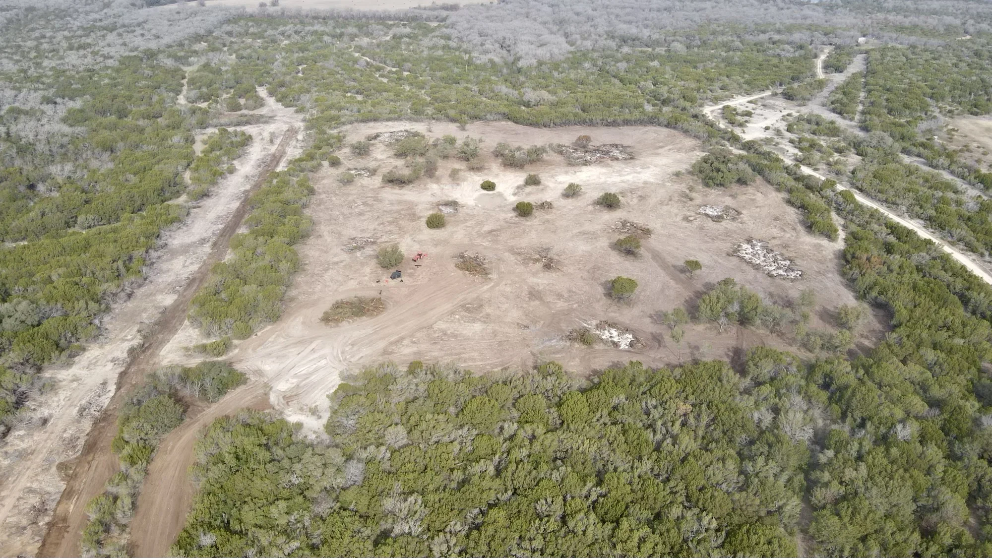 Aerial view of cleared land with selective tree removal, graded soil, and access roads surrounded by forest