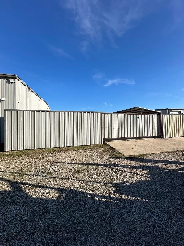 White corrugated metal fence with black steel frame and gate entry on gravel base